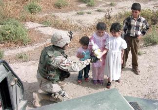 Photograph of an American soldier giving gifts to children in Iraq, taken by an American soldier of C Co, 1/252 Army Reserve Battalion . Logo for the M203.com presentation entitled Why.
