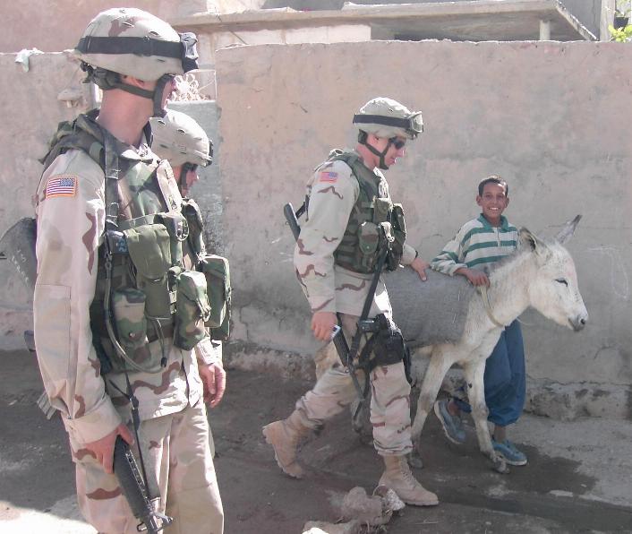 Photograph of teenager and his donkey walking with American soldiers in Iraq. Photograph by an American soldier of C Co, 1/252 Army Reserve Battalion. 
