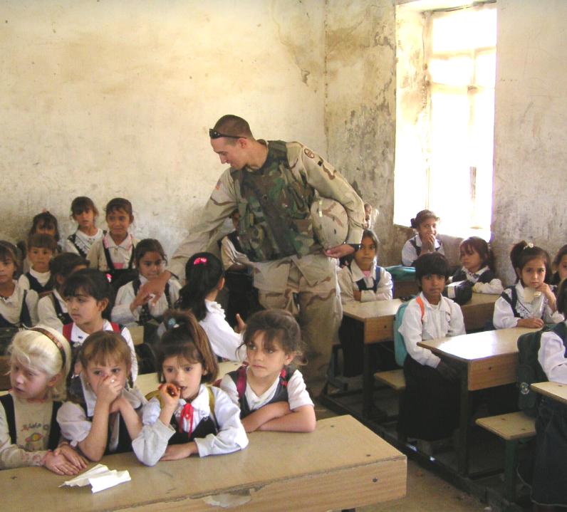 Photograph of Iraqi children in their class room and an American soldier visiting them. Photograph by an American soldier of C Co, 1/252 Army Reserve Battalion. 