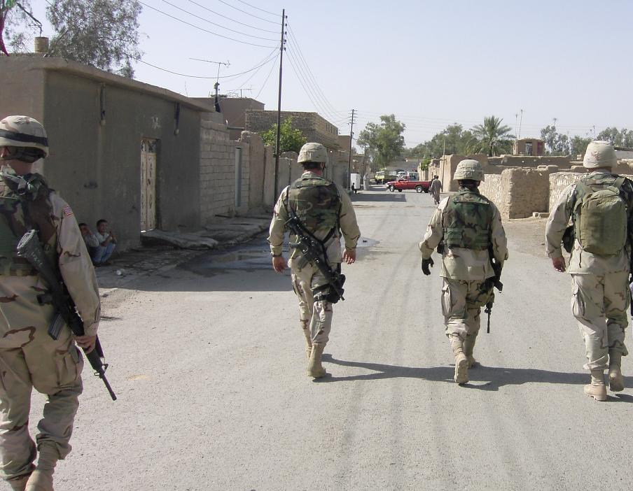 Photograph of four American soldiers walking away from the camera, down a street in Iraq. Photograph by an American soldier of C Co, 1/252 Army Reserve Battalion. 